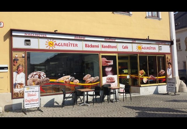 Au&szlig;enansicht der Caf&eacute;-B&auml;ckerei Naglreiter mit Tischen und St&uuml;hlen vor dem Gesch&auml;ft.