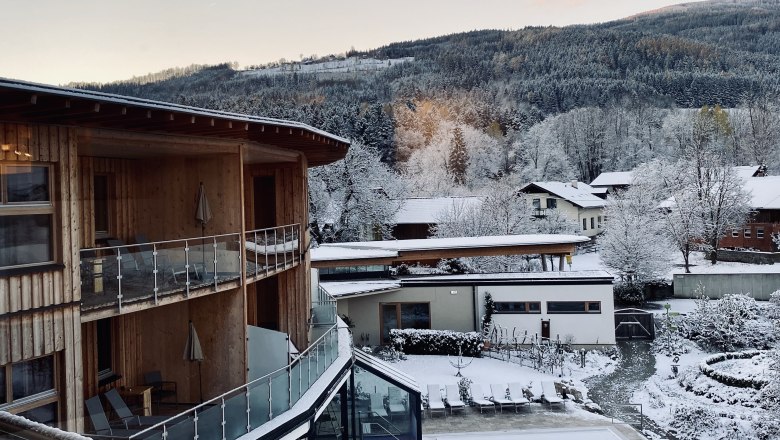 Winterliche Landschaft mit schneebedeckten Geb&auml;uden und B&auml;umen in den Bergen.