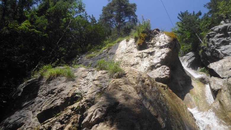 Felsiger Wasserfall mit B&auml;umen und blauem Himmel.