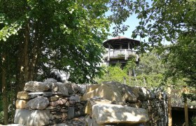 Aussichtsturm der Gartenschule Langenlois umgeben von B&auml;umen und einer Steinmauer.