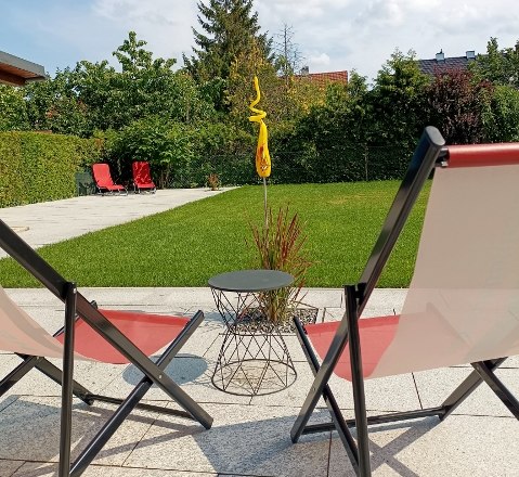 Zwei Liegest&uuml;hle im Garten mit Rasen und B&auml;umen im Hintergrund.