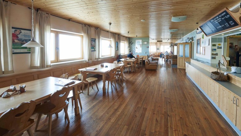 Heller Gastraum mit Holztischen, gro&szlig;en Fenstern und Bergblick.