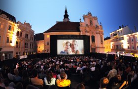 Open-Air-Kinoabend auf einem Platz mit vielen Zuschauern vor einer großen Leinwand.