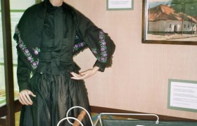 Eine Schaufensterpuppe in traditioneller Kleidung neben einem alten Kinderwagen in einem Ausstellungsraum.