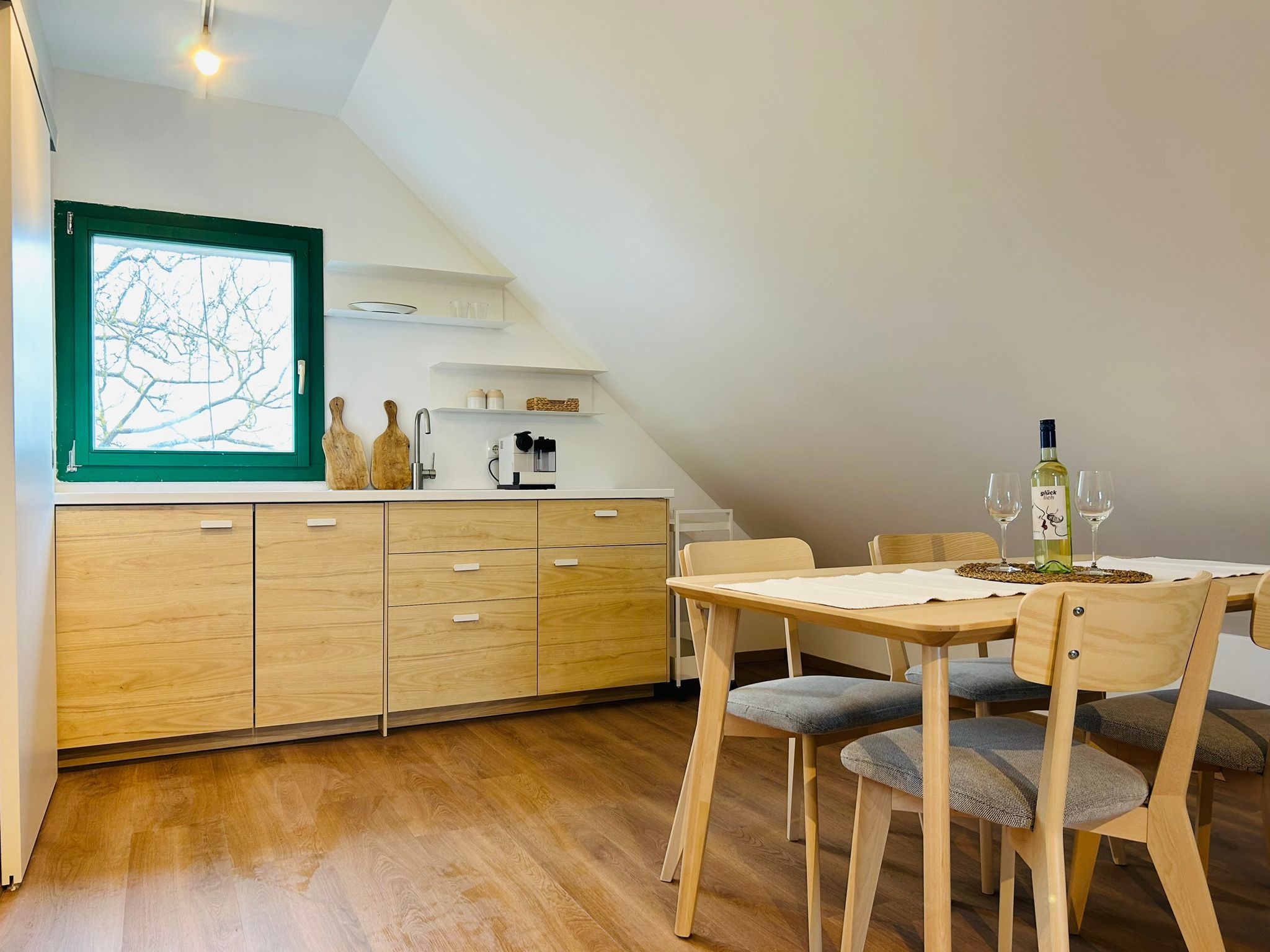 Moderne Küche mit Holzschränken, Esstisch und Stühlen, Fenster mit grünem Rahmen.