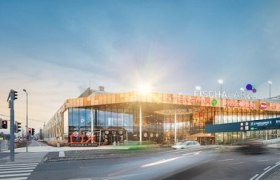 Vorderansicht des Einkaufszentrums Fischapark mit moderner Glasfassade und beleuchteten Schildern.