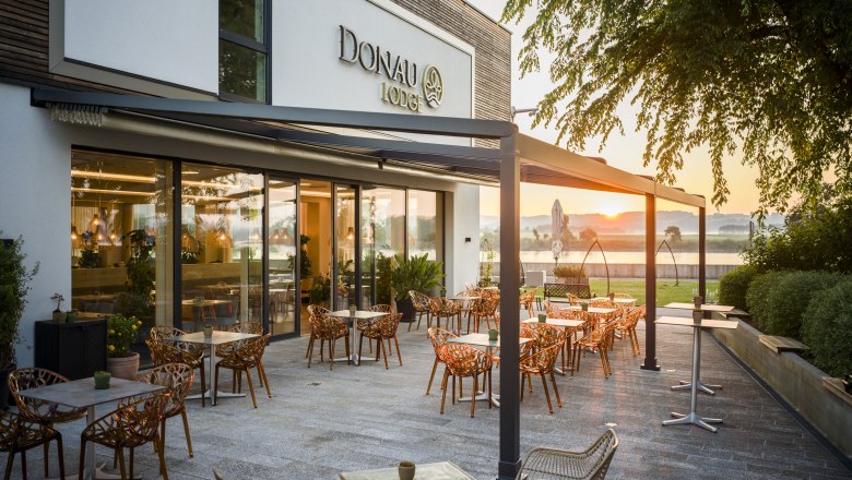 Terrasse der Donau Lodge Ybbs bei Sonnenuntergang mit Tischen und St&uuml;hlen.