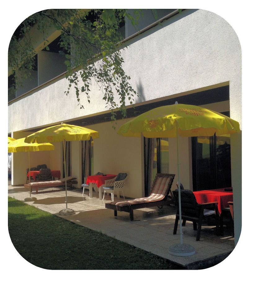 Terrasse mit gelben Sonnenschirmen und Liegestühlen vor einem Gebäude.