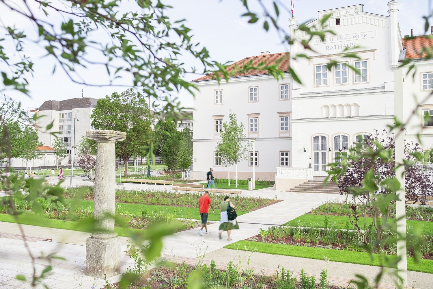 Menschen gehen auf Weg vor Rathaus Tulln umringt von Blumenbeeten 
