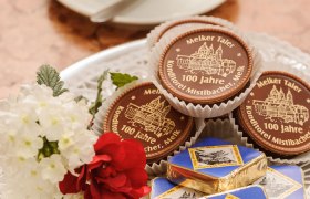 Ein Teller mit Pralinen und einer Tasse Kaffee im Hintergrund.