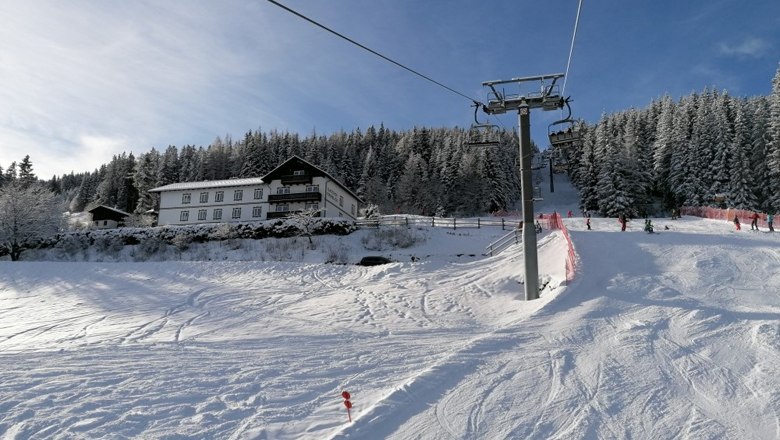 Schneebedeckte Skipiste mit Skilift und Wald im Hintergrund.
