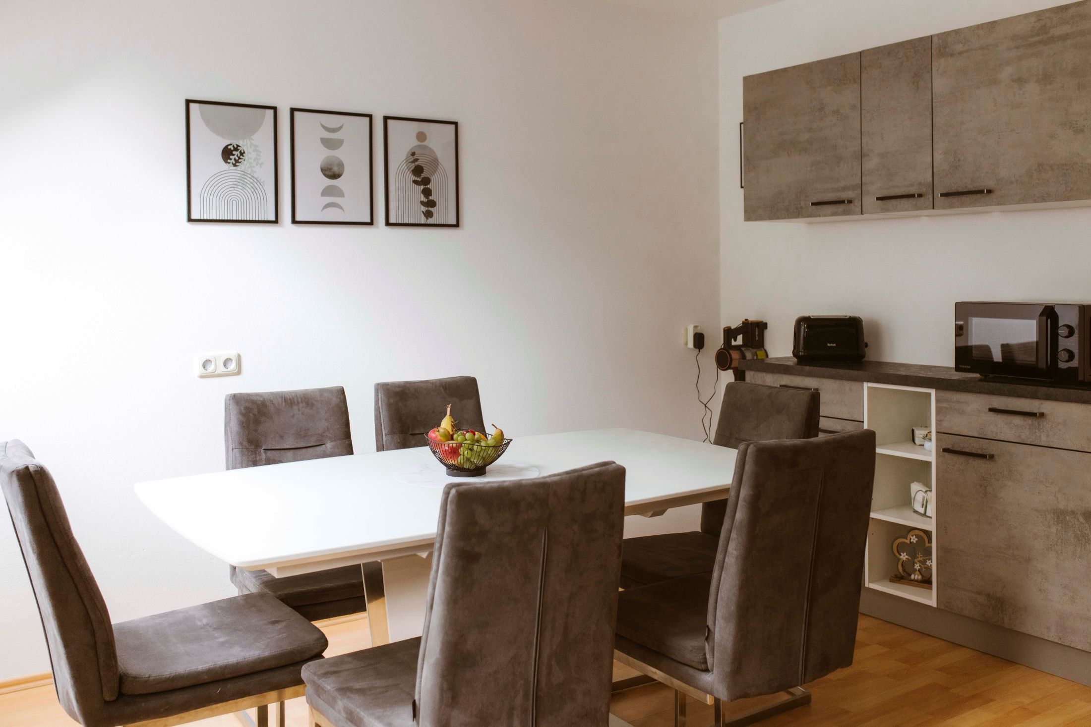 Moderner Essbereich mit grauen Stühlen, weißem Tisch und minimalistischer Dekoration.