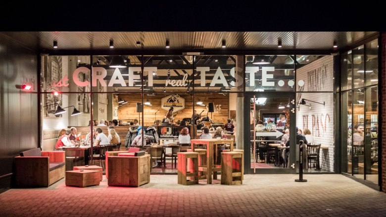 Au&szlig;enansicht eines Restaurants mit Glasfront, innen sitzen Menschen an Tischen.