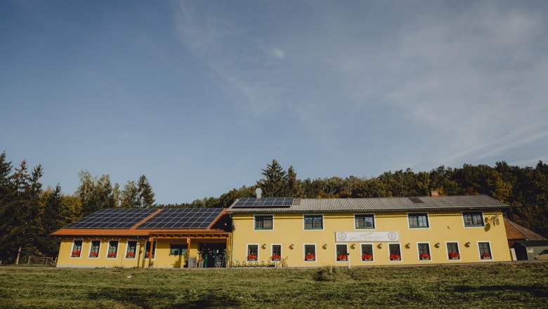 Gelbes Gebäude mit Solarpanelen auf dem Dach, umgeben von Bäumen.
