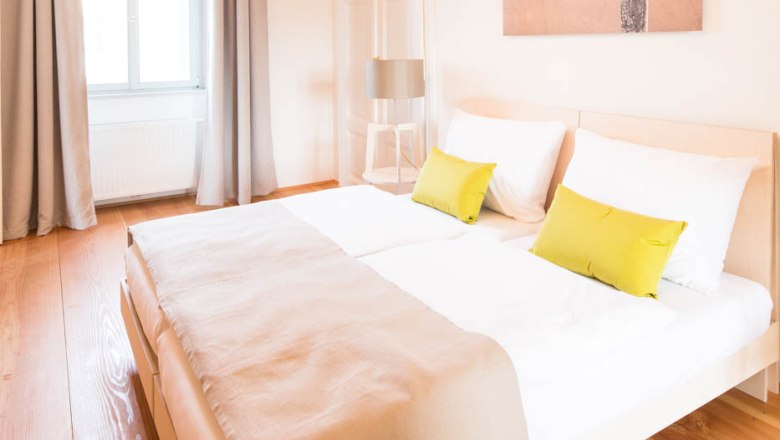 OBENauf, © OBENauf Helles Schlafzimmer mit Doppelbett, Holzboden und modernen Lampen.