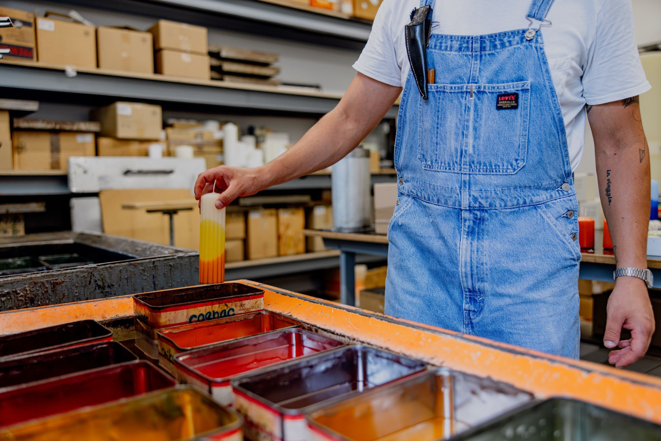 Person in Latzhose taucht Kerze in Farbbad.