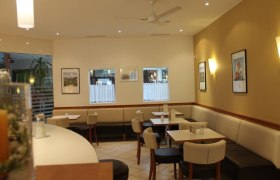 Innenansicht eines Caf&eacute;s mit Tischen, St&uuml;hlen und Wanddekorationen.