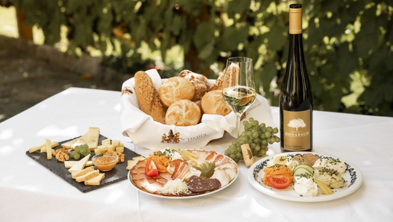 Heurigenjause mit Brot, Käse, Aufschnitt, Wein und Trauben auf einem Tisch.