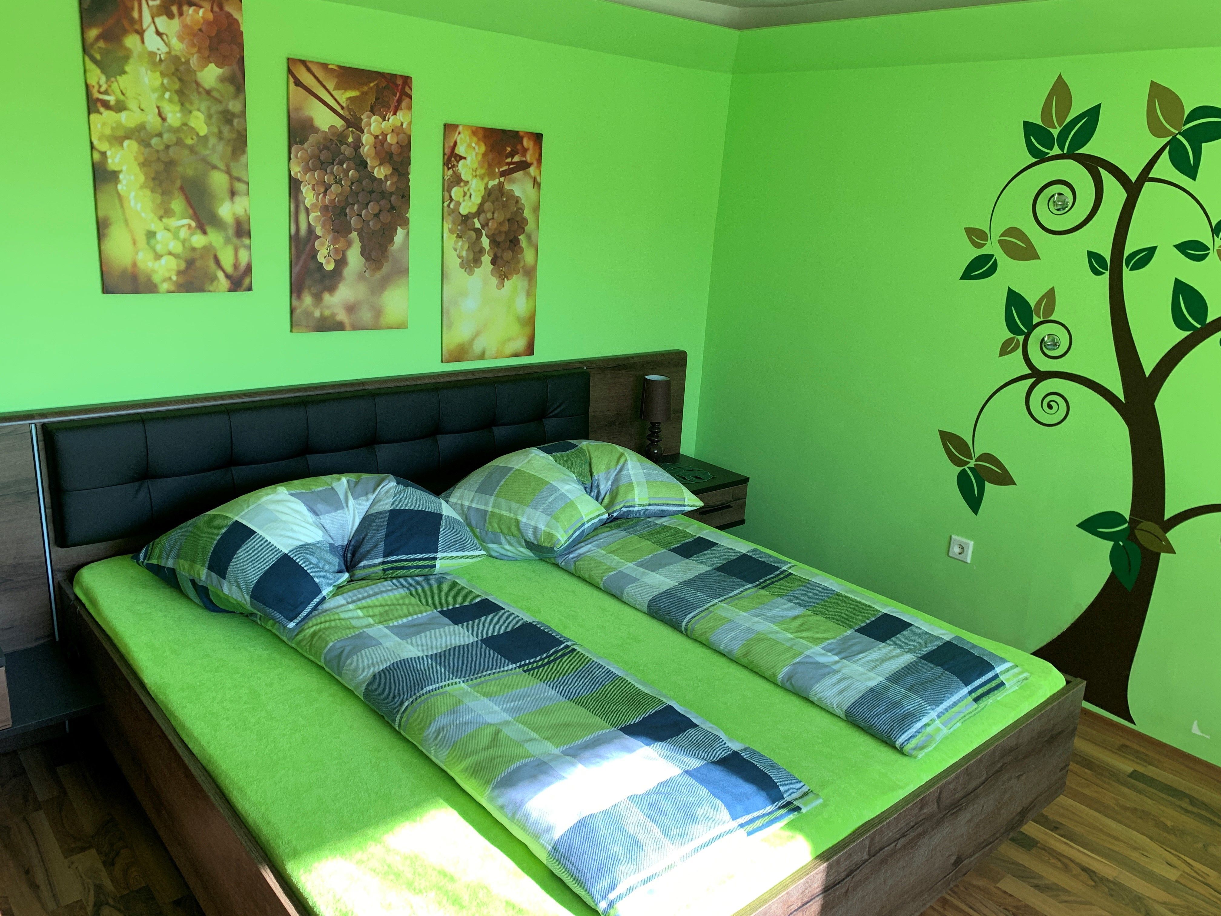 Schlafzimmer mit grünem Thema, Doppelbett, Wandbilder von Trauben und Baumdekoration.