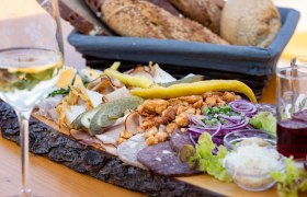 Heurigenplatte mit Aufschnitt, Zwiebeln, Gurken und Brot auf einem Holztisch.