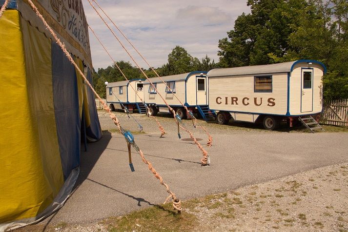 Zirkuswagen und Zelt auf einem Schotterplatz.