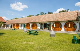 Ein Winzerhof mit runden Holzt&uuml;ren und gr&uuml;ner Wiese im Vordergrund.