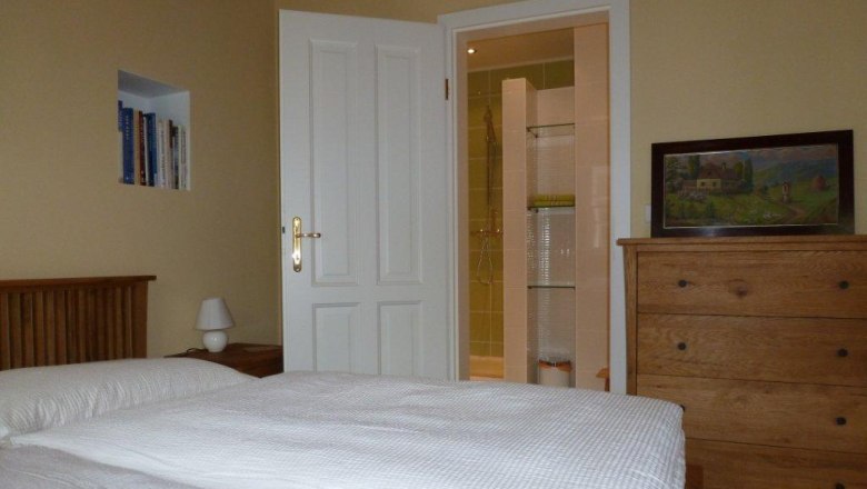 Ein gem&uuml;tliches Doppelzimmer mit Bett, Kommode, B&uuml;cherregal und offenem Bad.