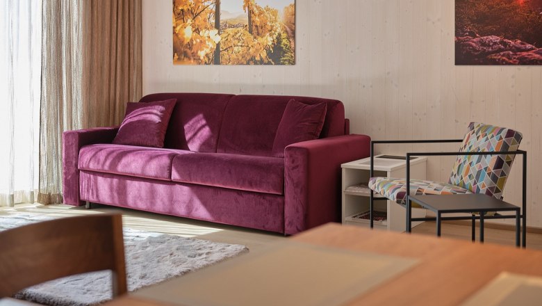 Wohnzimmer mit lila Sofa, buntem Stuhl und Wandbildern.