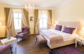 Elegantes Schlafzimmer mit Doppelbett, lila Akzenten und Kronleuchter.