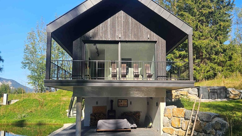 Walddenke, Hausansicht, © Mag. Plötzeneder Modernes Haus mit Holzfassade und Balkon, umgeben von Natur und einem kleinen Teich.