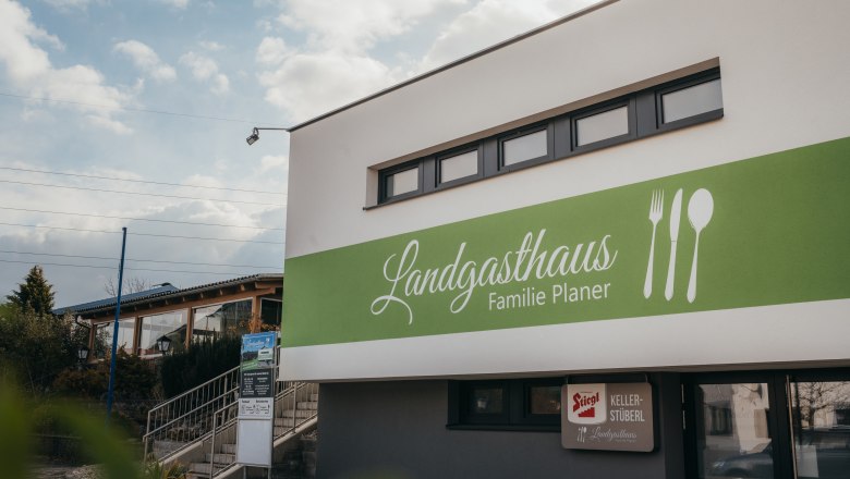 Au&szlig;enansicht des Landgasthauses Familie Planer mit gr&uuml;nem Schild und Bestecksymbolen.