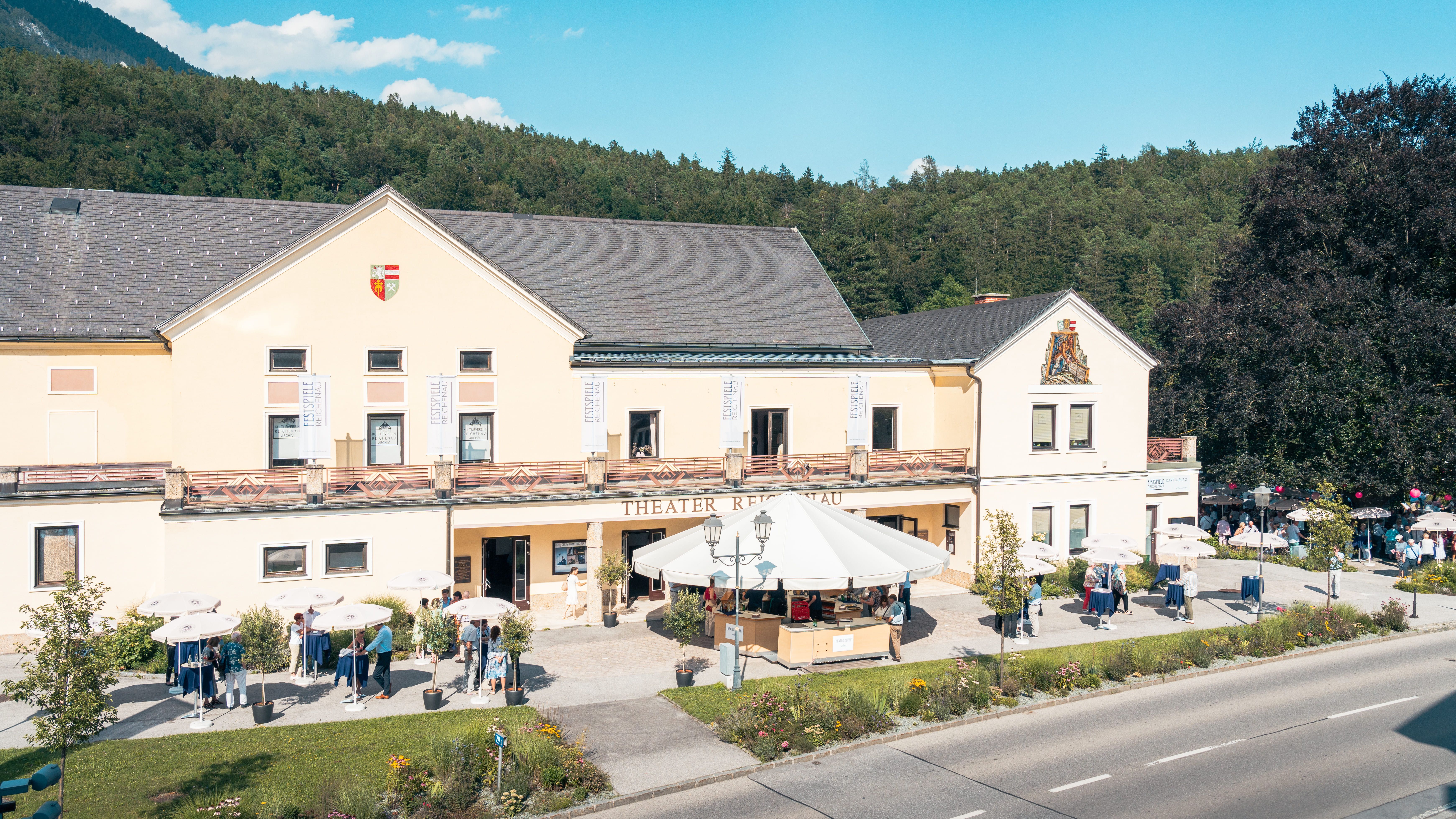 Theater Reichenau mit Menschen und Sonnenschirmen davor.