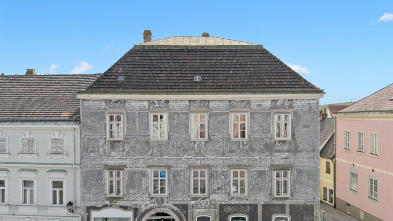 Historisches Geb&auml;ude mit grauer Fassade und dekorativen Malereien in einer Stadt.