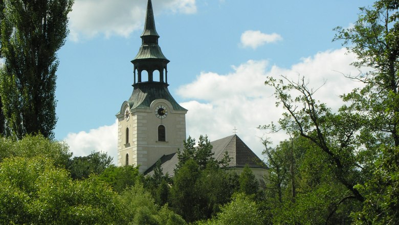 Kirchturm in Dobersberg umgeben von B&auml;umen und blauem Himmel.