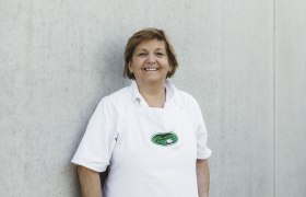 Frau in weißer Schürze vor grauer Wand.