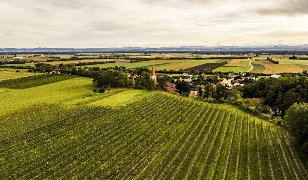 Luftaufnahme einer ländlichen Landschaft mit Feldern, einem Dorf und einer Kirche mit rotem Turm.