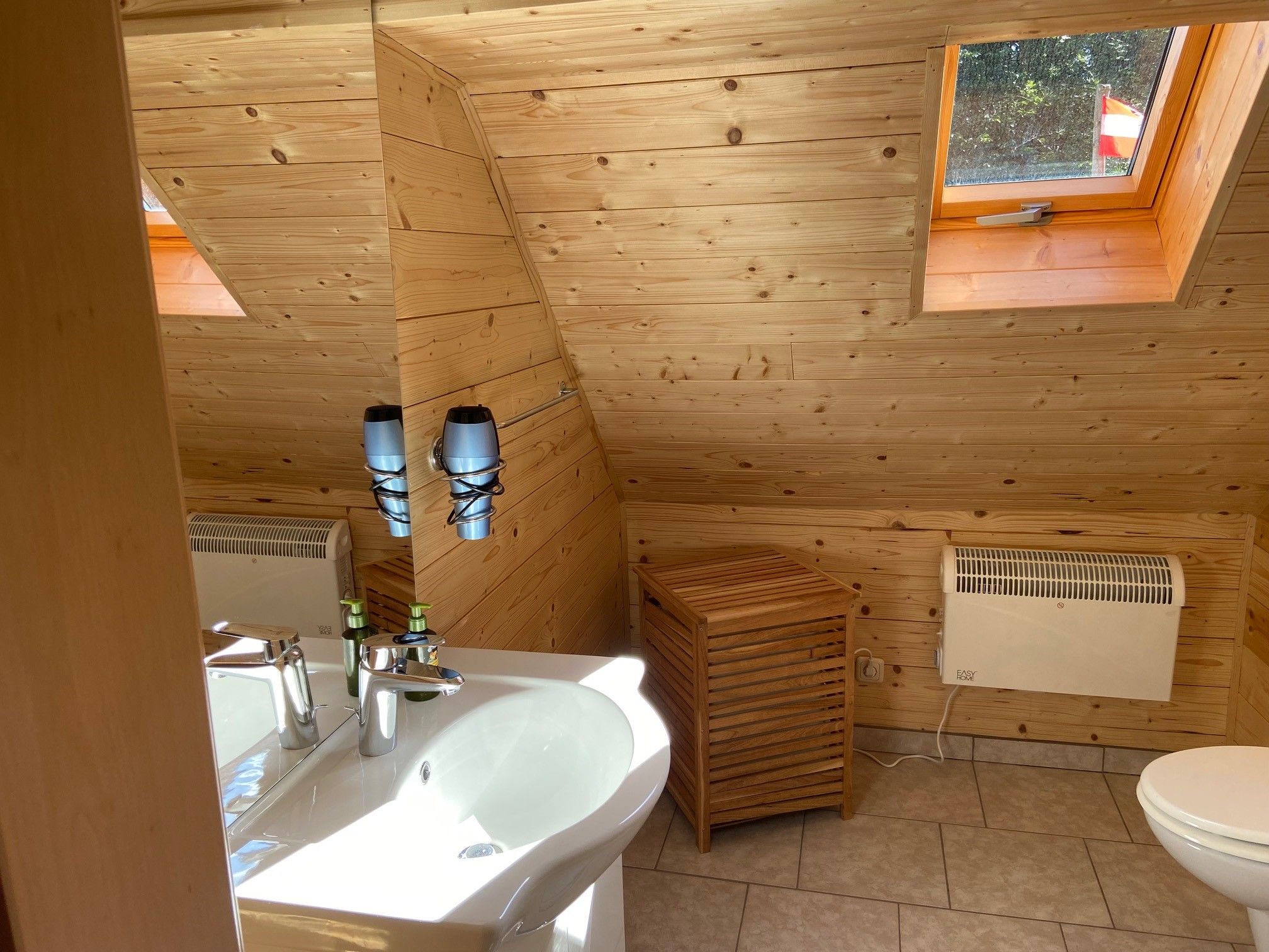 Holzvertäfeltes Badezimmer mit Waschbecken, Spiegel, Dachfenster und Heizkörper.