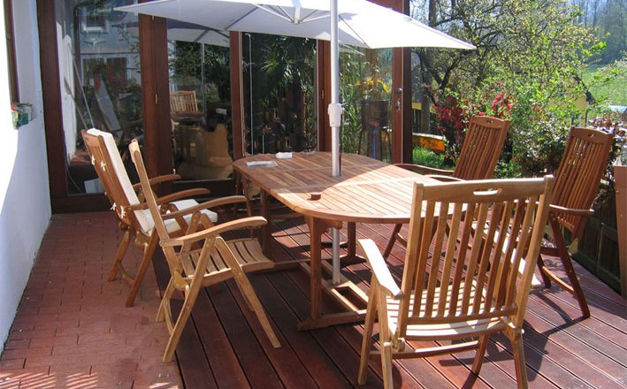 Holzterrasse mit Tisch, Stühlen und Sonnenschirm.