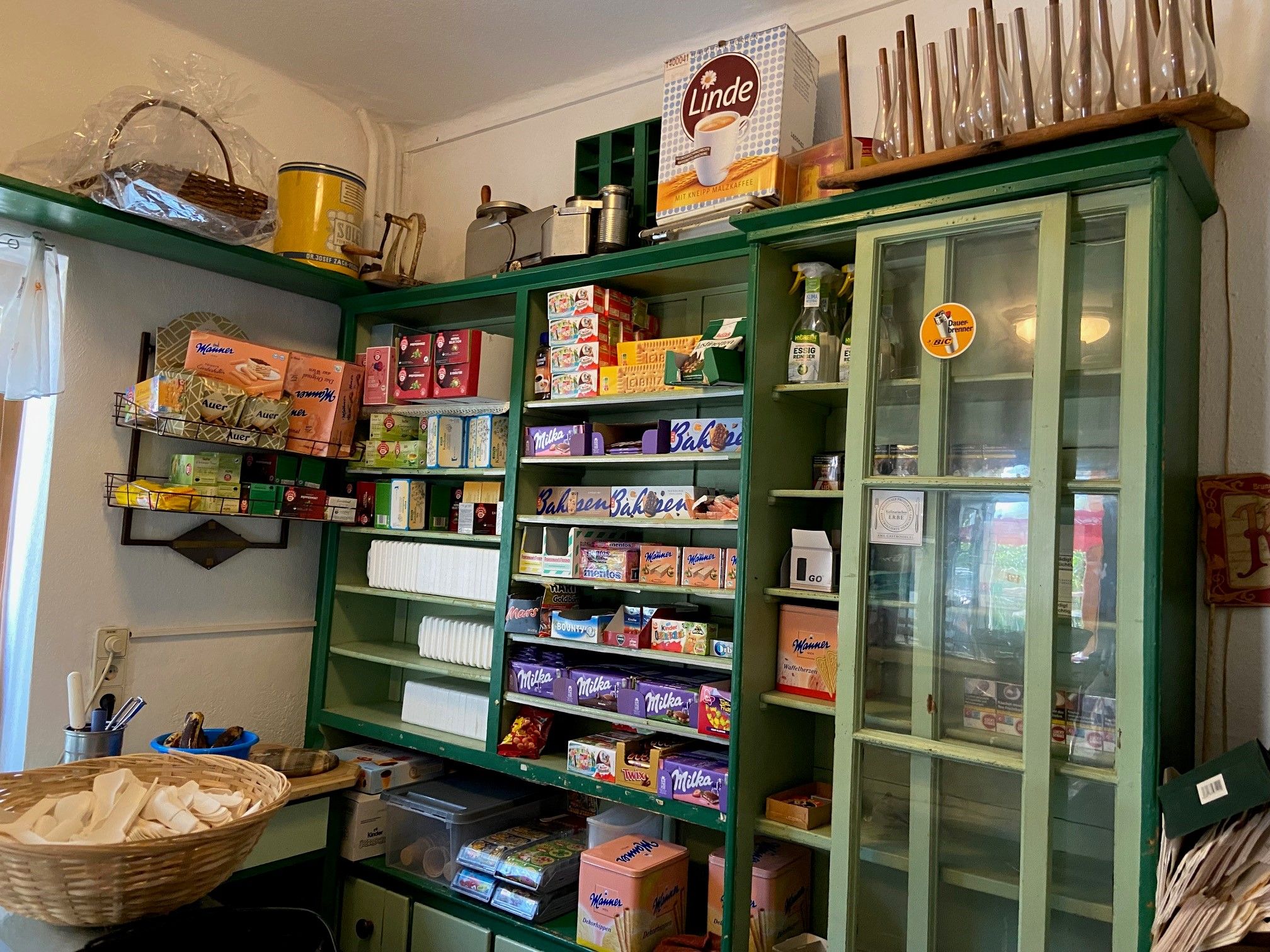 Ein traditioneller Laden mit grünen Regalen, gefüllt mit verschiedenen Lebensmitteln und Haushaltswaren.