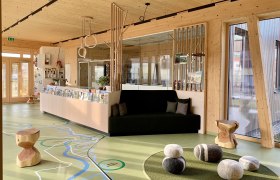 Innenansicht eines modernen Foyers mit Holzelementen, einer Sitzbank und dekorativen Steinen auf dem Boden.