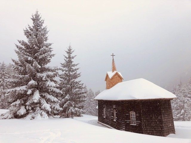 Eine kleine Kirche im Schnee mit Tannenbäumen im Hintergrund.