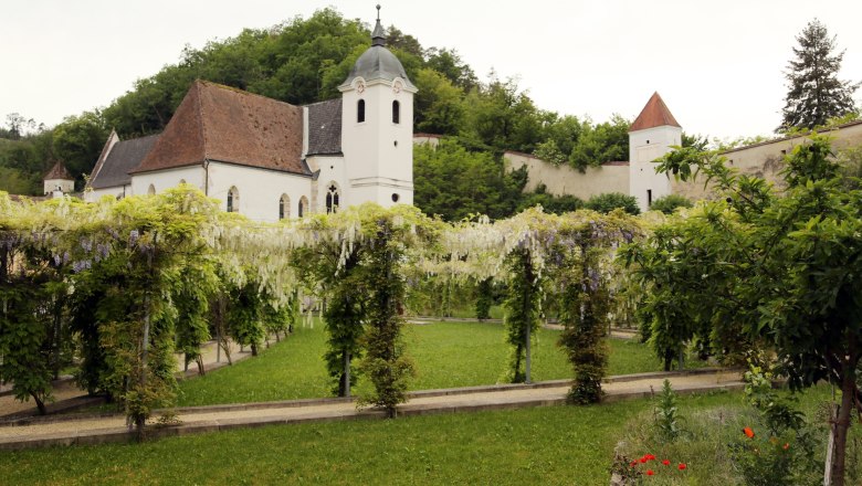 Blick auf eine historische Kartause mit Garten und Pergola.