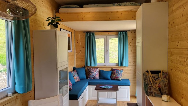 Kleiner Wohnbereich mit Hubbett, blauen Vorh&auml;ngen und Holzw&auml;nden.