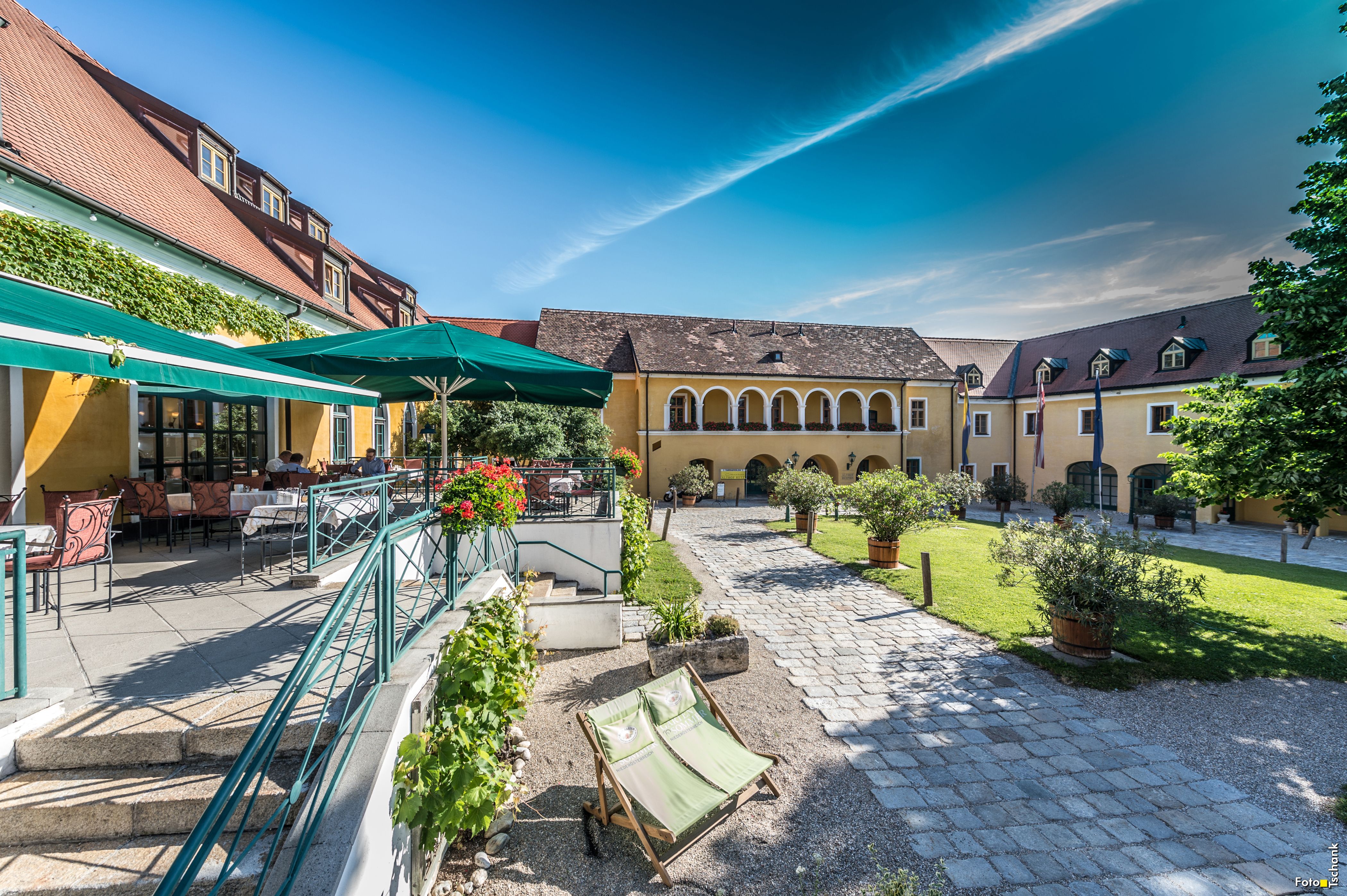 Ein malerischer Innenhof mit gelben Gebäuden, Terrassenbereich und Sonnenschirmen.