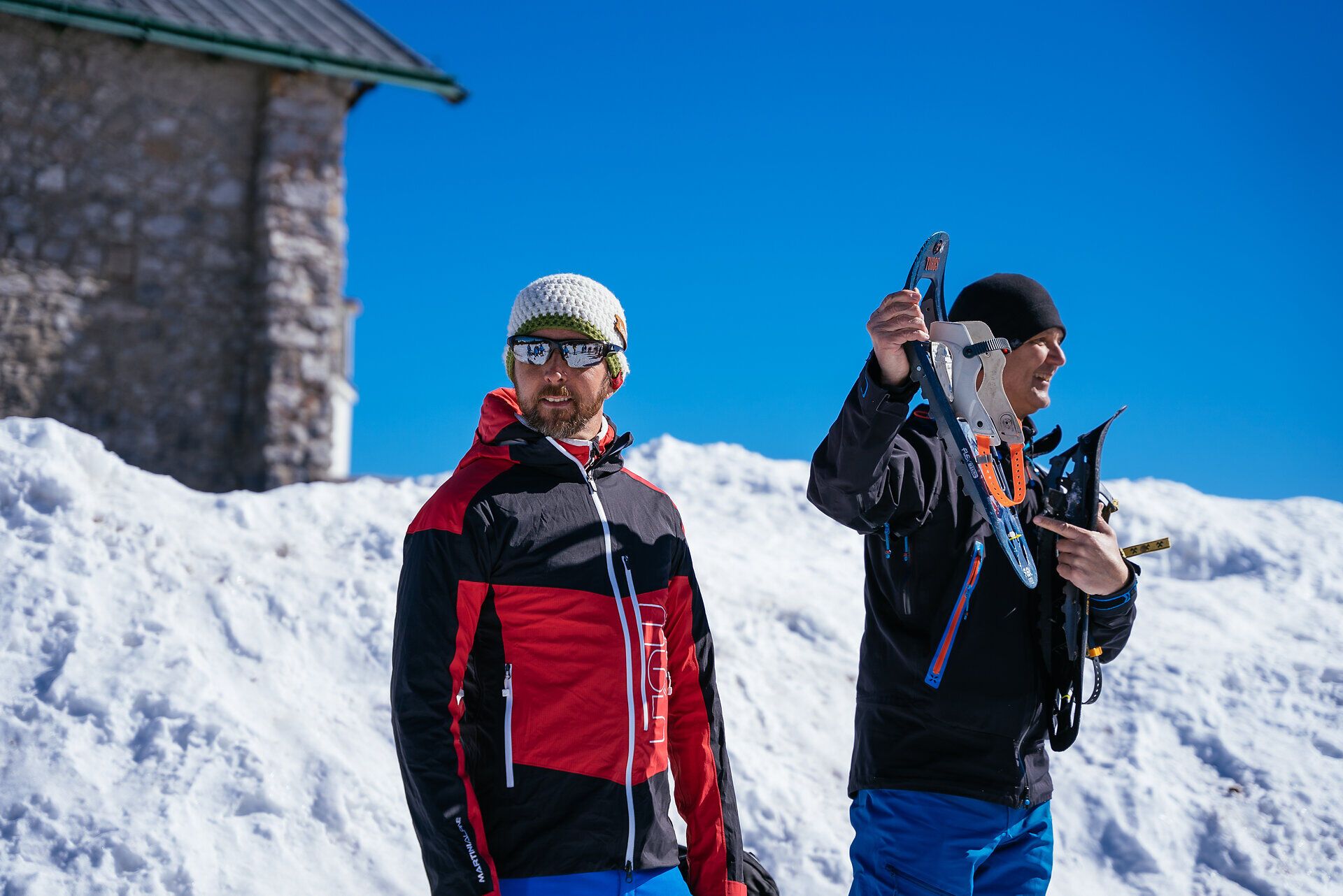 Wolfgang Menzel und Gruppe von Menschen mit Schneeschuhen wandert auf verschneiter Fläche vor Nadelbäumen unter blauem Himmel
