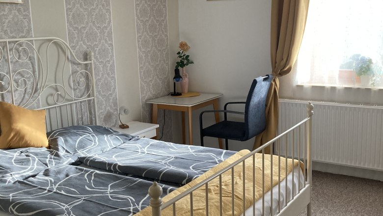 Gem&uuml;tliches Schlafzimmer mit Doppelbett, gelben Vorh&auml;ngen und dekorativer Tapete.