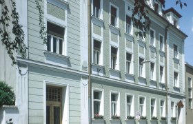 Außenansicht eines mehrstöckigen Gebäudes mit grüner Fassade und weißen Fensterrahmen.