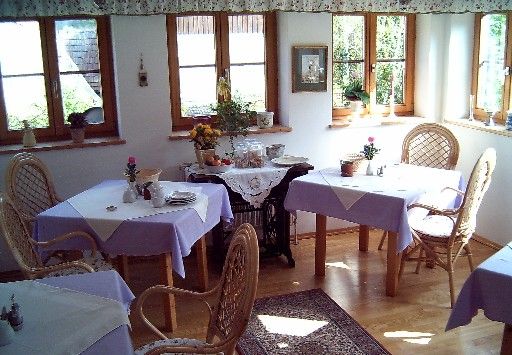 Gemütlicher Frühstücksraum mit Korbstühlen und lila Tischdecken.