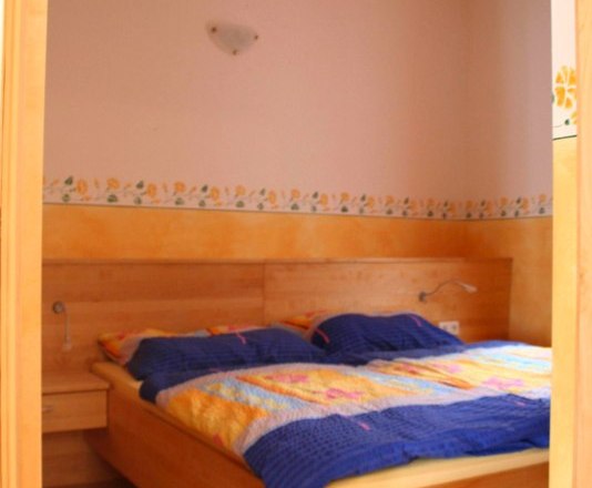 Schlafzimmer mit Holzbett und bunter Bettw&auml;sche.