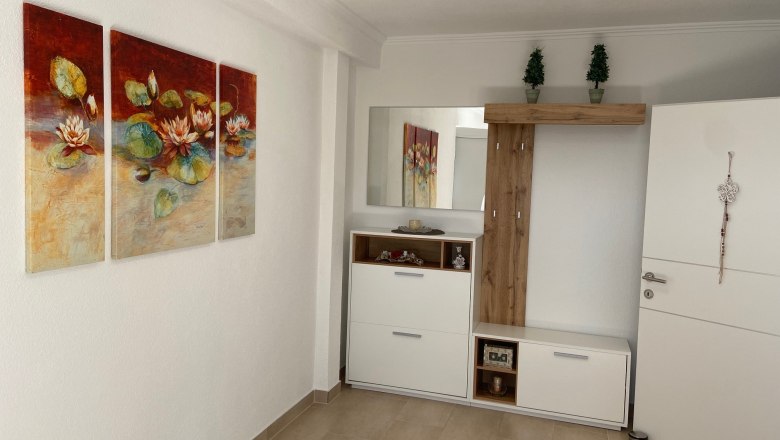 Ein Vorraum mit einem dreiteiligen Seerosenbild an der Wand, einem weißen Schrank mit Spiegel und Dekorationen.